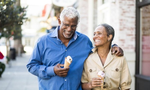 older couple walks down city sidewalk while holding ice cream cones